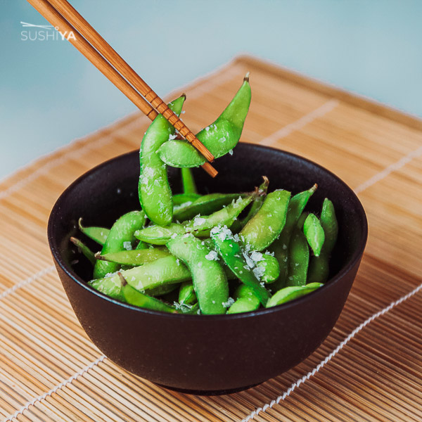 Na obrázku sa medzi paličkami a v čienej miske nachádzajú Edamame. Ide o nezrelé, vylúpané sojové bôby